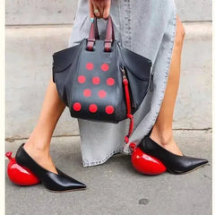 Women's black leather pointed toe pumps with unique red balloon-shaped heels, stylishly paired with a designer handbag.
