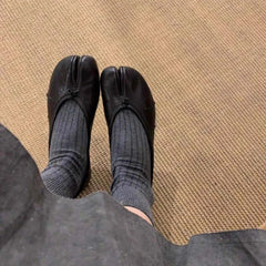 luxury split toe women's pumps paired with gray socks on a textured floor background.